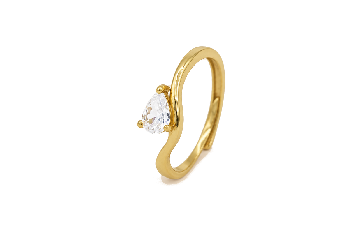 Anello con pietra a goccia, finitura dorata e pietra chiara, sfondo beige